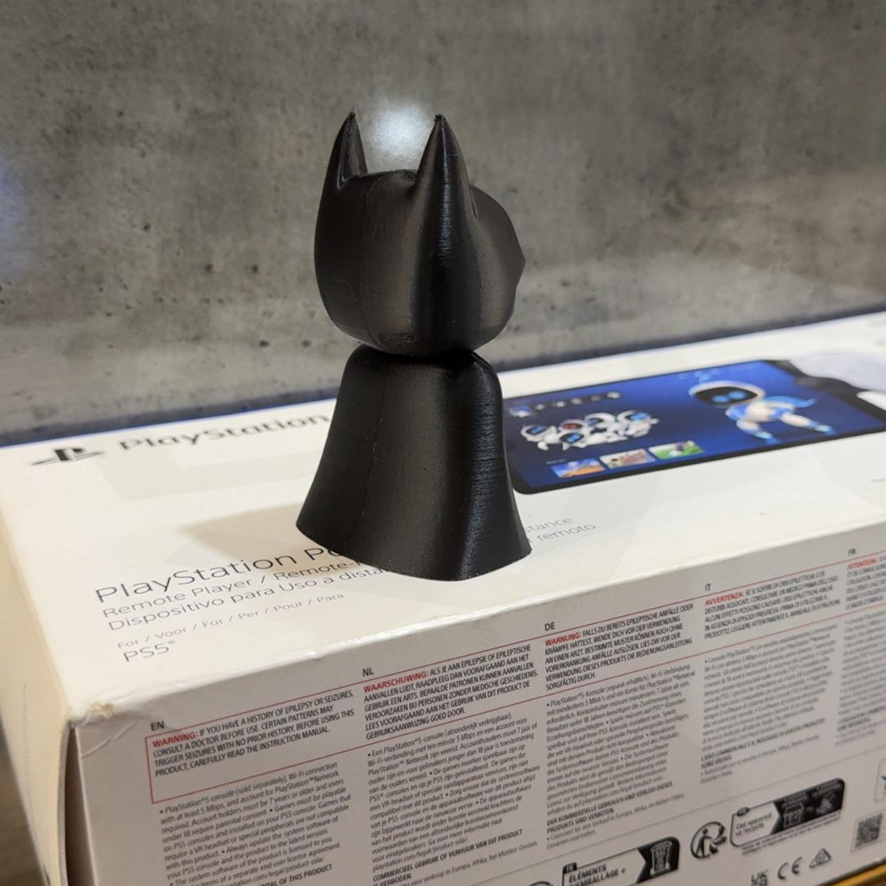 Black cat-shaped object on a PlayStation 4 console box with a concrete wall background