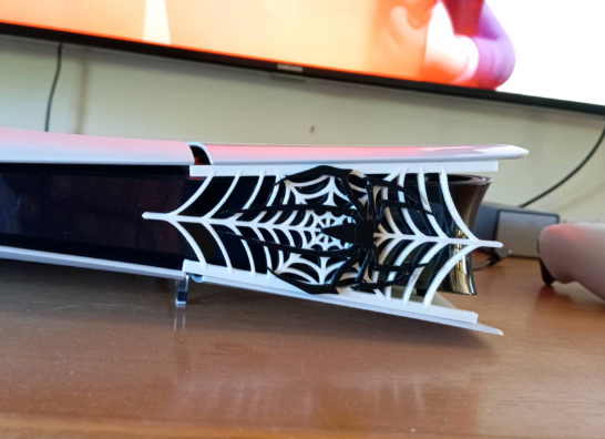 ps5 with a spider web design on a stand, placed on a wooden surface.