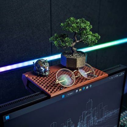 A wooden desktop organizer tray with a grid of small pegs holds a bonsai tree, round eyeglasses, and a small robot head figurine, positioned above a computer monitor in a dark gaming setup with RGB lighting.